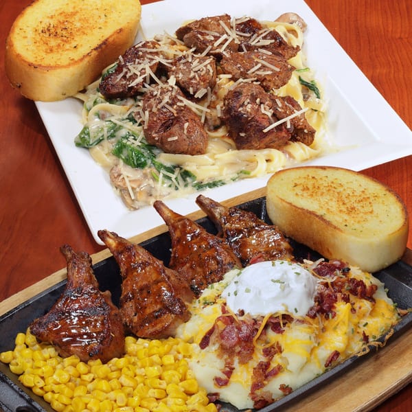 Two plates of food: one with steak tips over pasta, the other with lamb chops, corn, and loaded mashed potatoes.