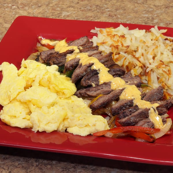 A red plate holds scrambled eggs, steak with cheese sauce, and hash browns.