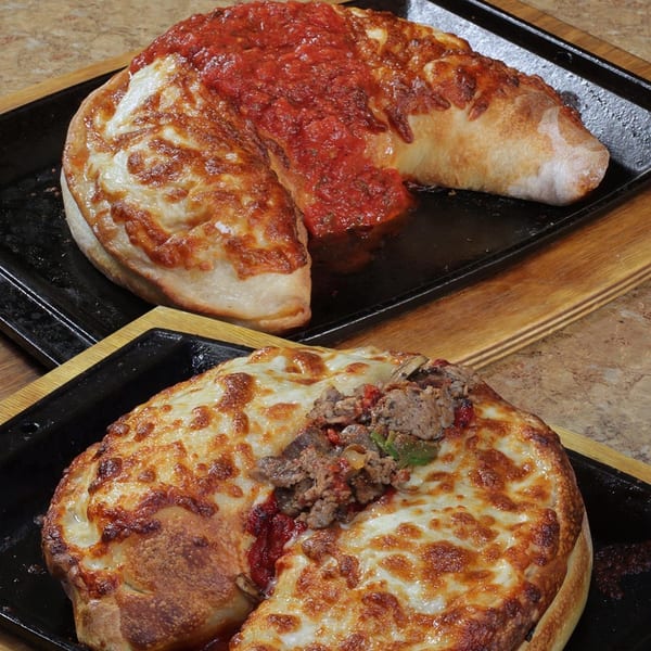 Two baked calzones, one with red sauce, the other with meat and cheese, on black trays.